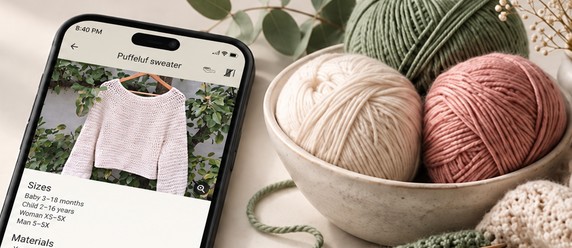 Knit My Size on a phone, showing a crochet sweater pattern, next to a bowl of yarn